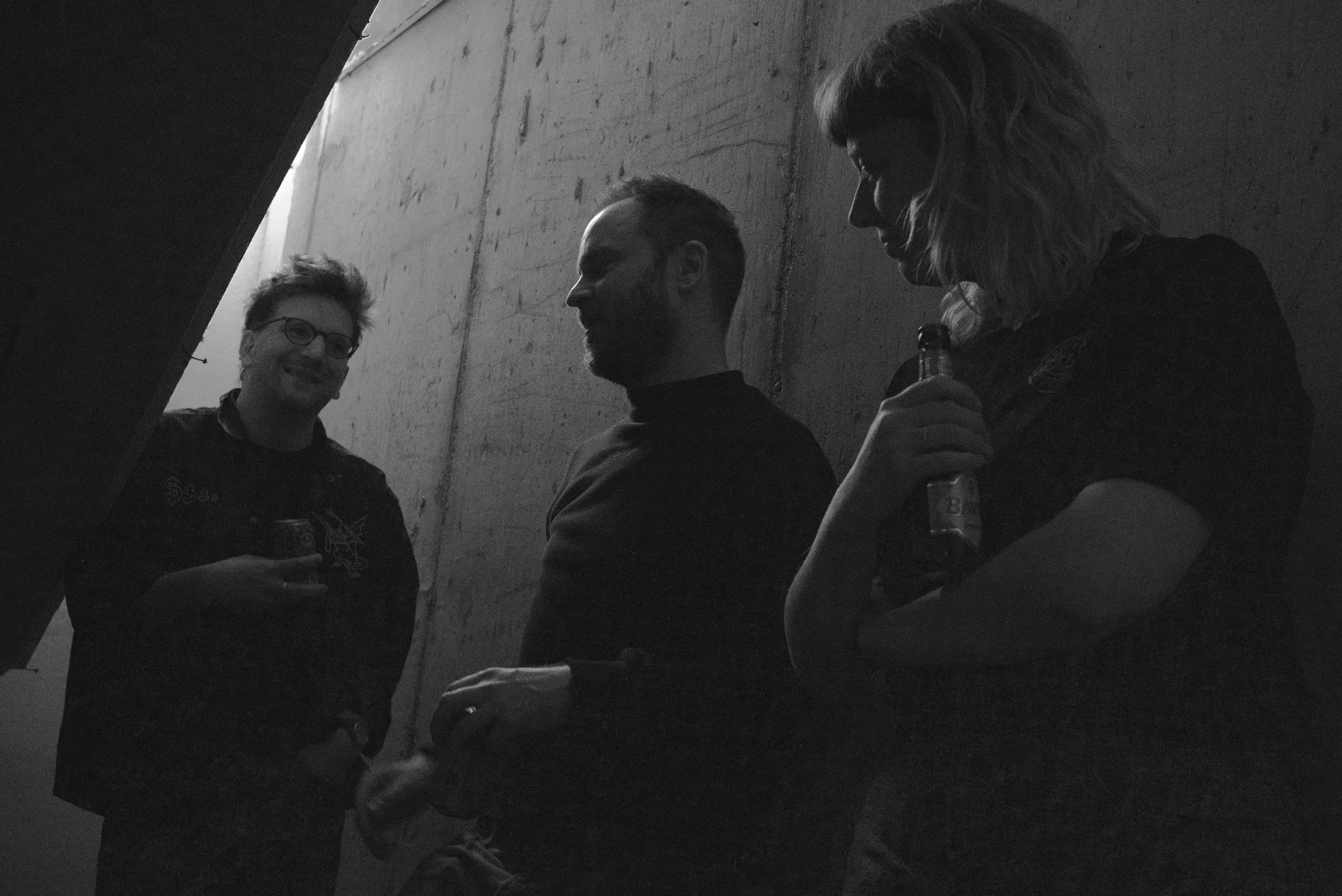 The three members of Grondstof talking in a dim concrete hallway.